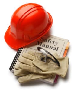Red helmet with pair of work gloves laying on top of a Safety Manual book.